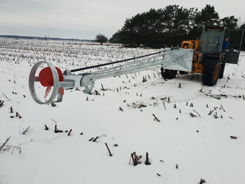Hydraulisk gödselomrörare kopplad till lastmaskin på snötäckt fält.